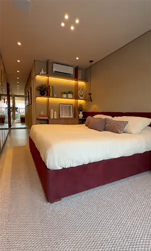 Quarto amplo com cama estofada em tom vinho e iluminação aconchegante